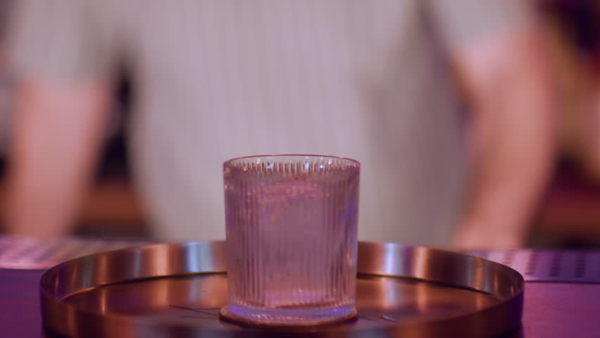 Refreshing beverage. Preparing alcohol drink. Barman opening liquor bottle. Wide crystal glass with big ice cube on metal tray counter.