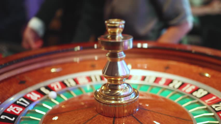 Casino table with roulette wheel in motion, with casino chips, tokens, the hand of croupier, dollar money and a group of gambling rich people playing bet on a party, blue poker table and deck of cards
