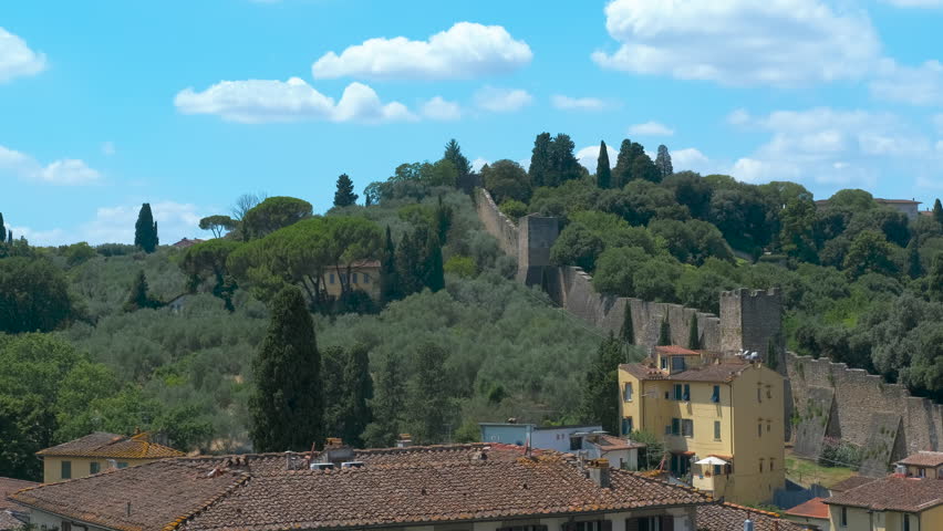 Panoramic view of florence showing walls and roofs. Panoramic cityscape revealing historic florence walls and terracotta rooftops surrounded by verdant greenery under luminous blue summer sky