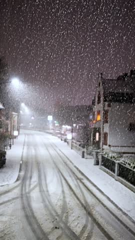 silent snowcovered street, nighttime winter scene with snowfall, calm winter night with drifting snow and glowing windows, serene snowy street illuminated by ambient glow and gentle falling