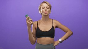 Woman holding green juice bottle with mouth in o and hand on hip against purple studio backdrop; confidence wellness. - Powered by Shutterstock - Get 15% off with code: PIKWIZARD15