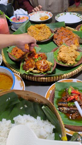 Rainy atmosphere at traditional Indonesian restaurant with joglo design, featuring a woven bamboo platter filled with Nusantara dishes, creating a cozy and authentic dining scene.