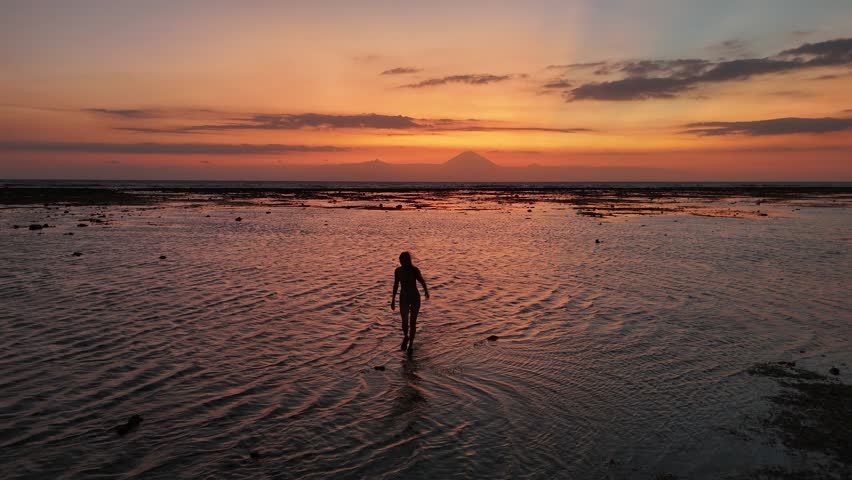 Aerial view of a young girl walking in the water at sunset with Mount Agung in the background, Gili Trawangan, Indonesia