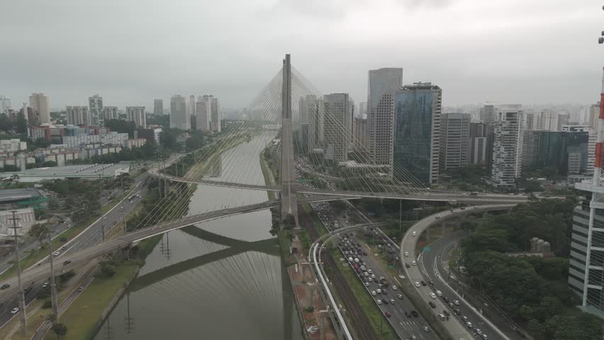 4K drone footage showing the Octávio Frias de Oliveira cable-stayed bridge crossing the Pinheiros River in São Paulo, Brazil. Captured on a clear day with city skyline and traffic movement. Ideal for 