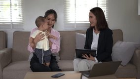 A woman is holding a baby while sitting on a couch. Another woman is sitting next to them, looking at a tablet. The scene appears to be a casual and friendly gathering between the two women - Powered by Shutterstock - Get 15% off with code: PIKWIZARD15
