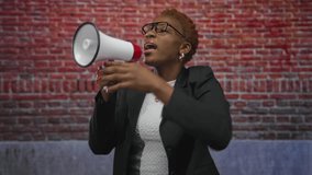 Young african american woman shouting into a megaphone against a red brick building while raising her fist and wearing glasses; empowerment advocacy solidarity activism. - Powered by Shutterstock - Get 15% off with code: PIKWIZARD15