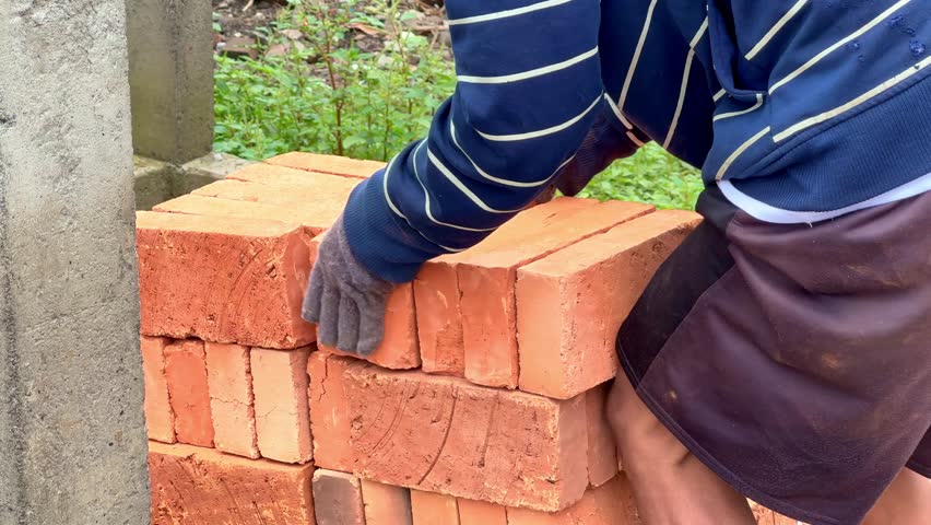 Close up of a worker arranging red clay bricks by hand at a construction site. Manual building material preparation.