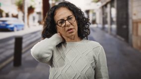 Woman with curly hair in a sweater experiencing neck pain outdoors in a city street. - Powered by Shutterstock - Get 15% off with code: PIKWIZARD15