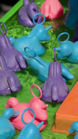 Plastic unicorn figures float in water, vibrant sunlight, playful carnival atmosphere, close-up camera movement