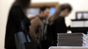 Stack of spiral notebooks on registration table with blurred people in background during business seminar or conference indoors in modern corporate environment. - Powered by Shutterstock - Get 15% off with code: PIKWIZARD15
