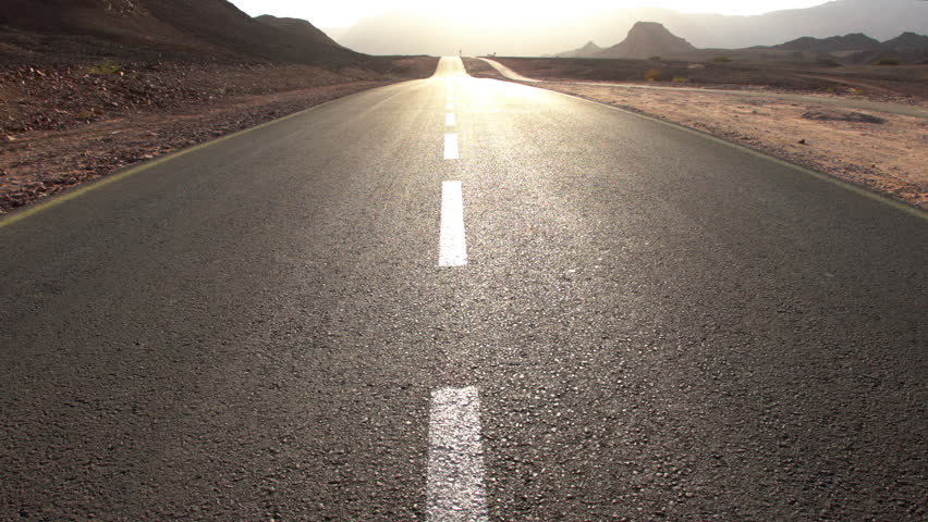 View of an asphalt road running through a desert landscape with sandstone formations in Timna National Park. Israel. Road trip. Road at sunset.