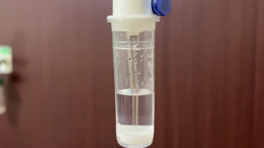 A close-up view of a transparent tube of infusion filled with clear liquid, showing small air bubbles clinging to the inner walls, against a soft brown background.