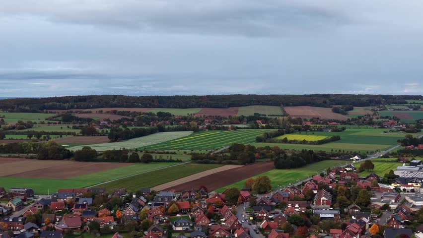 Aerial lateral shot of European houses and homes in rural area of USA. Orange colored tiles on roof. Wet agricultural farm fields on hillside. Dusk with clouds in autumn. Wide shot.