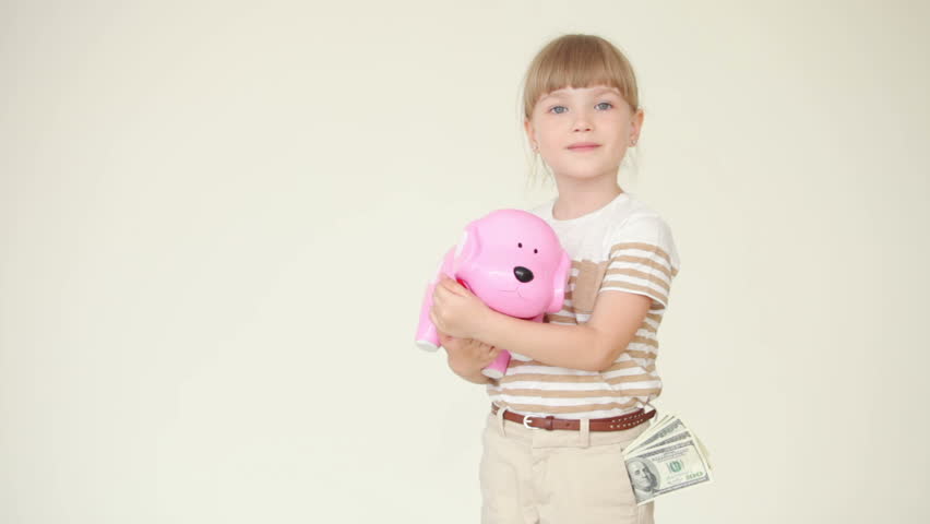 Little girl is standing and holding a piggy bank with coins
