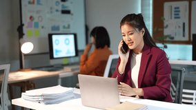 Young professional Asian businesswoman working late at night in a modern office, multitasking by talking on the phone and using her laptop to meet a deadline with her colleague - Powered by Shutterstock - Get 15% off with code: PIKWIZARD15