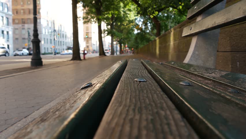 Wooden bench near Central Park in New York City, United States. Cars and people on street in Manhattan, USA. Defocused perspective. Yellow taxi cab on road.