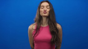 Young hispanic woman in a pink tank top sending a kiss gesture with her lips in a studio setting; affection. - Powered by Shutterstock - Get 15% off with code: PIKWIZARD15