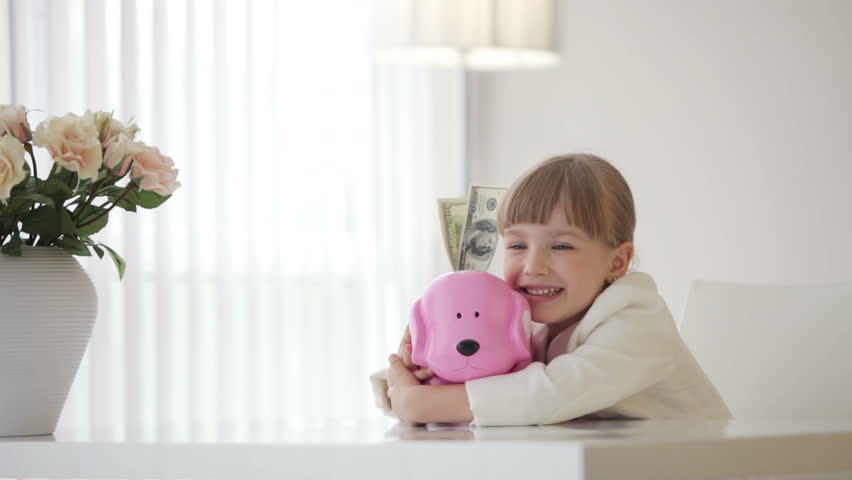 Little girl hugging a piggy bank with money
