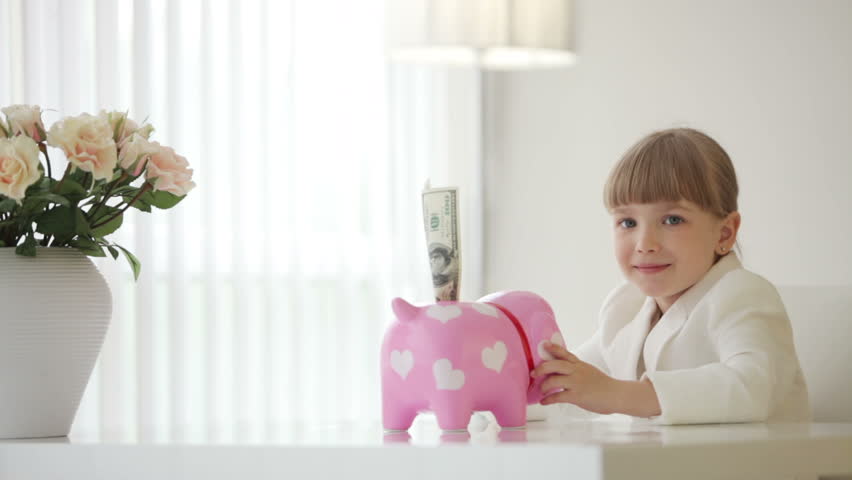 Girl sitting at the table and hugging  piggy bank
