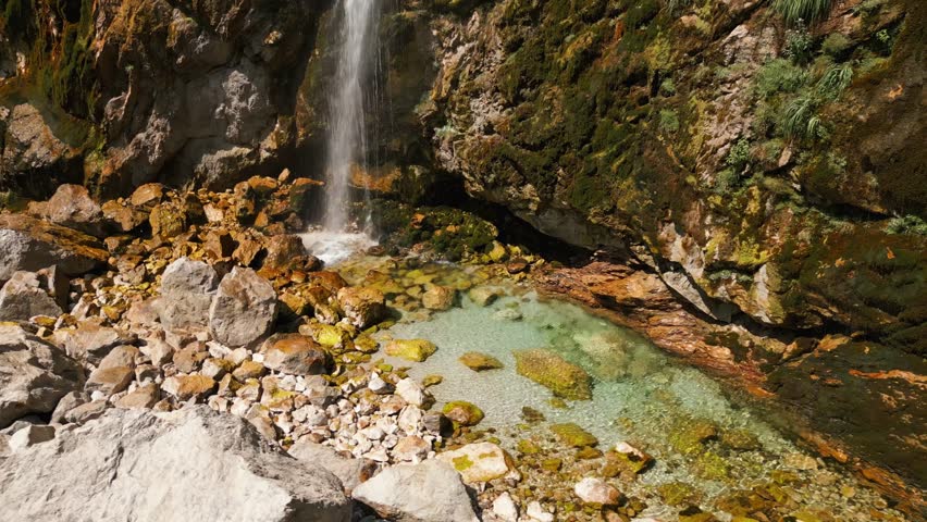 Clear mountain waterfall flowing over mossy rocks into a turquoise pool in Albania. Peaceful and natural landscape perfect for travel or nature footage.