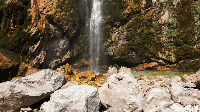 Clear mountain waterfall flowing over mossy rocks into a turquoise pool in Albania. Peaceful and natural landscape perfect for travel or nature footage.