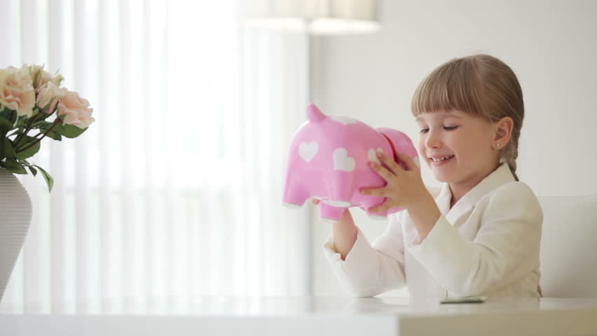 Girl sitting at table and holding piggy bank
