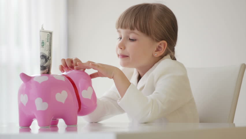 Little business woman sitting at a desk with piggy bank
