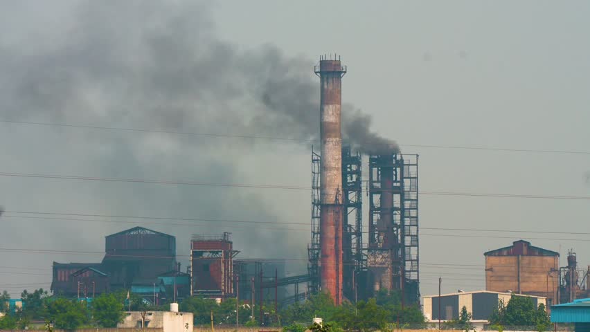 Very dense black smoke is coming out of the chimney of a big industrial site. Air pollution due to the black smoke of a big manufacturing plant or factory in India.
