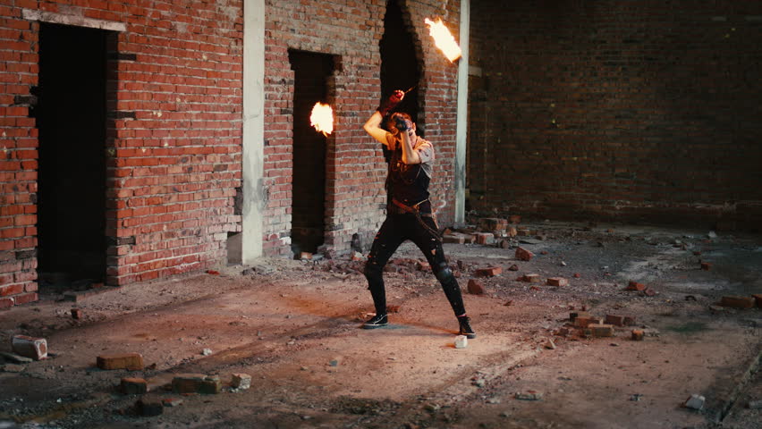 Young female fire dancer performing a mesmerizing show with burning poi, spinning the flaming torches in a dark, abandoned brick building, creating a beautiful and dangerous spectacle