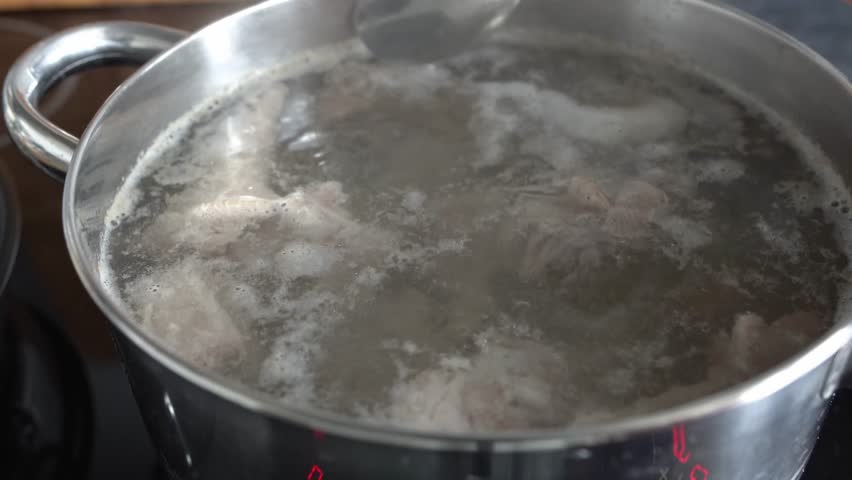 An unidentified woman skims a pot of boiling meat. Making meat broth.