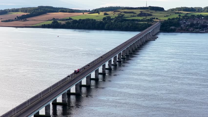 Drone footage shows cars traveling across Tay Road Bridge over river toward Dundee, Scotland, daytime