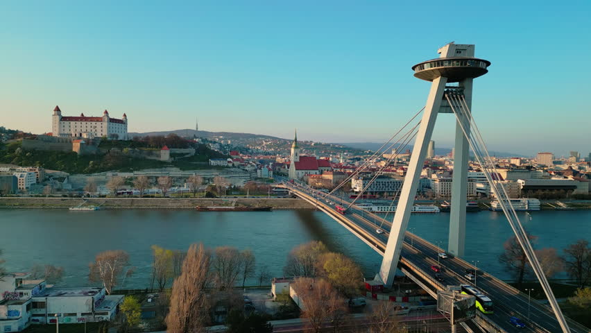 A drone footage of Slovakia, Bratislava with Most SNP bridge, Bratislava Castle and the old town buildings with roads under blue sky in spring