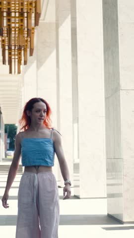A portrait of a teenage girl with red hair posing for a photo near columns at the entrance to a business center