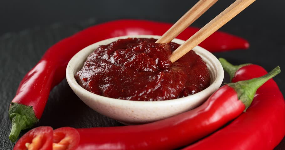 Bowl with spicy gochujang paste and fresh chili peppers. Close-up shot of chopsticks taking gochujang paste.