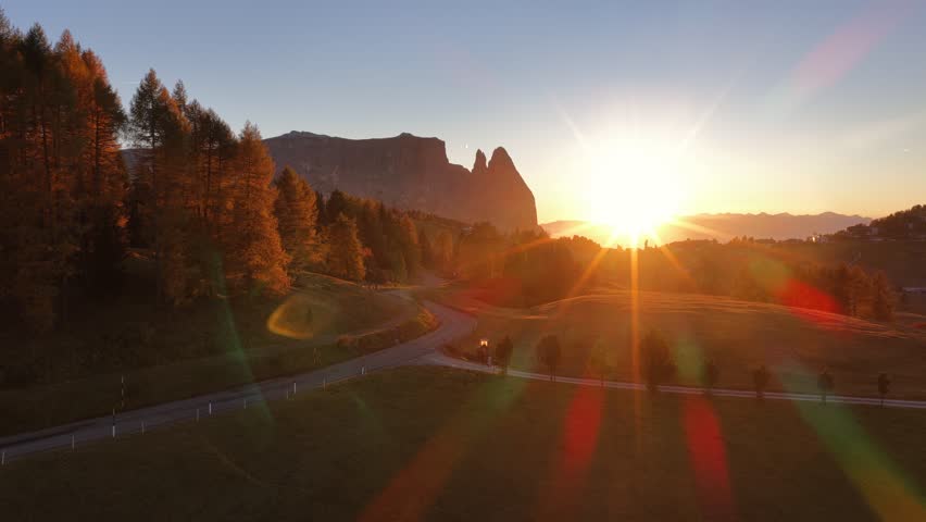 A drone view of Alpe di Siusi in South Tyrol, Italy, showing autumn meadows, golden larch trees, and the Schlern peaks glowing under the sunrise