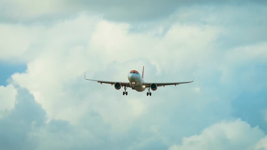 Jet flying with landing gear extended against cloudy sky background. Airliner approaching runway with wheels down through white clouds. Passenger aircraft descending in daylight with extended landing