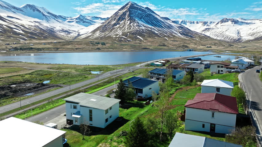 Aerial shot of Siglufjordur, North Iceland. Modern homes and fishing docks beneath dramatic mountain landscape near Akureyri.