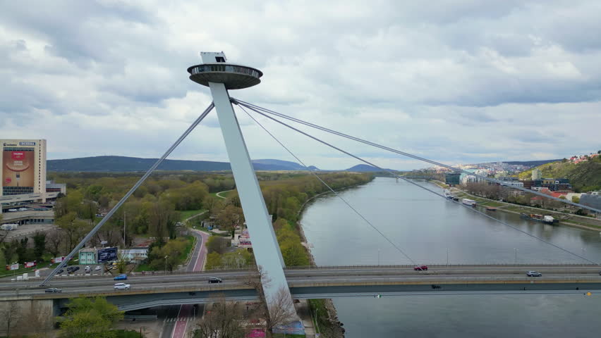 A timelapse aerial view of UFO Bridge Most SNP crossing Danube River in Bratislava Slovakia with hills and roads below