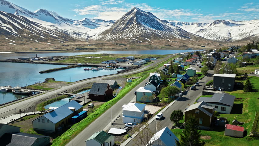 Drone view of Siglufjordur fjord near Akureyri, Iceland. Scenic harbor town with colorful houses, snow-capped peaks, and blue Arctic waters.