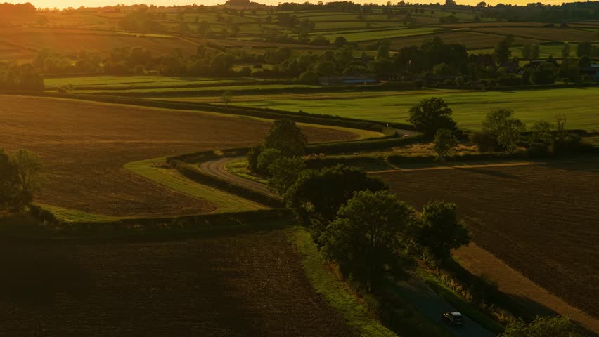 Multiple cars traveling along winding countryside road during golden sunset. Traveling countryside, road trip driving, enjoying sunset view. Vehicles moving through rural curved roadway in warm