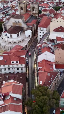 A vertical drone view of Lisbon's Alfama district showing red rooftops and the yellow tram 28 line running through the narrow streets in Portugal