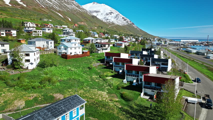 Colorful hillside houses of Siglufjordur, North Iceland. Drone view over fjord village and snowy peaks near Akureyri.