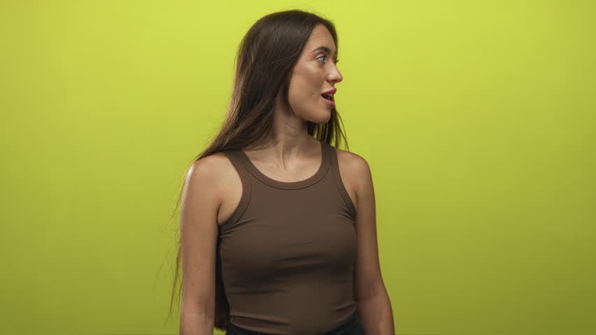 Woman with mouth open looking right in studio lit against lime green seamless wall, wearing brown tank top showing shoulder and long hair, casual portrait pose; curiosity.