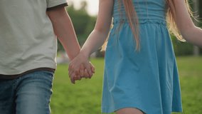 lower view of teenagers holding hands walking through playground grass, casual summer afternoon, friendship bond, relaxed sunlit park stroll, youthful connection, outdoor leisure, cheerful motion - Powered by Shutterstock - Get 15% off with code: PIKWIZARD15