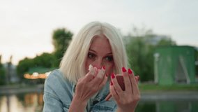 elegant woman sitting on riverside bridge in park during sunset uses compact mirror and white cloth to gently remove bright pink paint from nose after playful painting activity outdoors - Powered by Shutterstock - Get 15% off with code: PIKWIZARD15