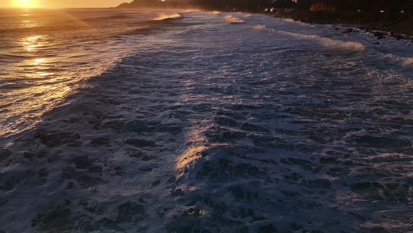 Aerial view of the golden sunset reflecting off the waves crashing along the coastline, creating a beautiful contrast, Cape Town, Western Cape, South Africa.