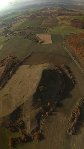 A vertical high-angle aerial view of Cicov Hill with long evening shadows over the surrounding farmland in the Czech Republic