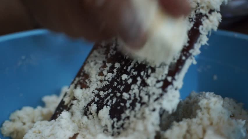 Close-up of a person manually grating cassava using a traditional grater, showing authentic Indonesian food preparation