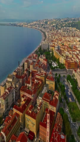  Aerial view of bustling beachfront promenade on sunny day. Beautiful panorama in Nice, France. Palm trees, old houses in old town azure sea and green hills. Summer in French Riviera