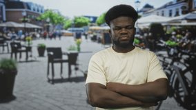 Young african american man with arms crossed and grimace in busy street cafe with outdoor tables and bicycles; anger defiance. - Powered by Shutterstock - Get 15% off with code: PIKWIZARD15